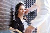 Photo of a woman receiving an assessment from an audiologist in a room lined with acoustic panels 